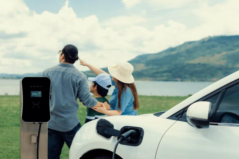 Foto van familie die kijkt naar het landschap terwijl hun elektrische auto aan de laadpaal zit